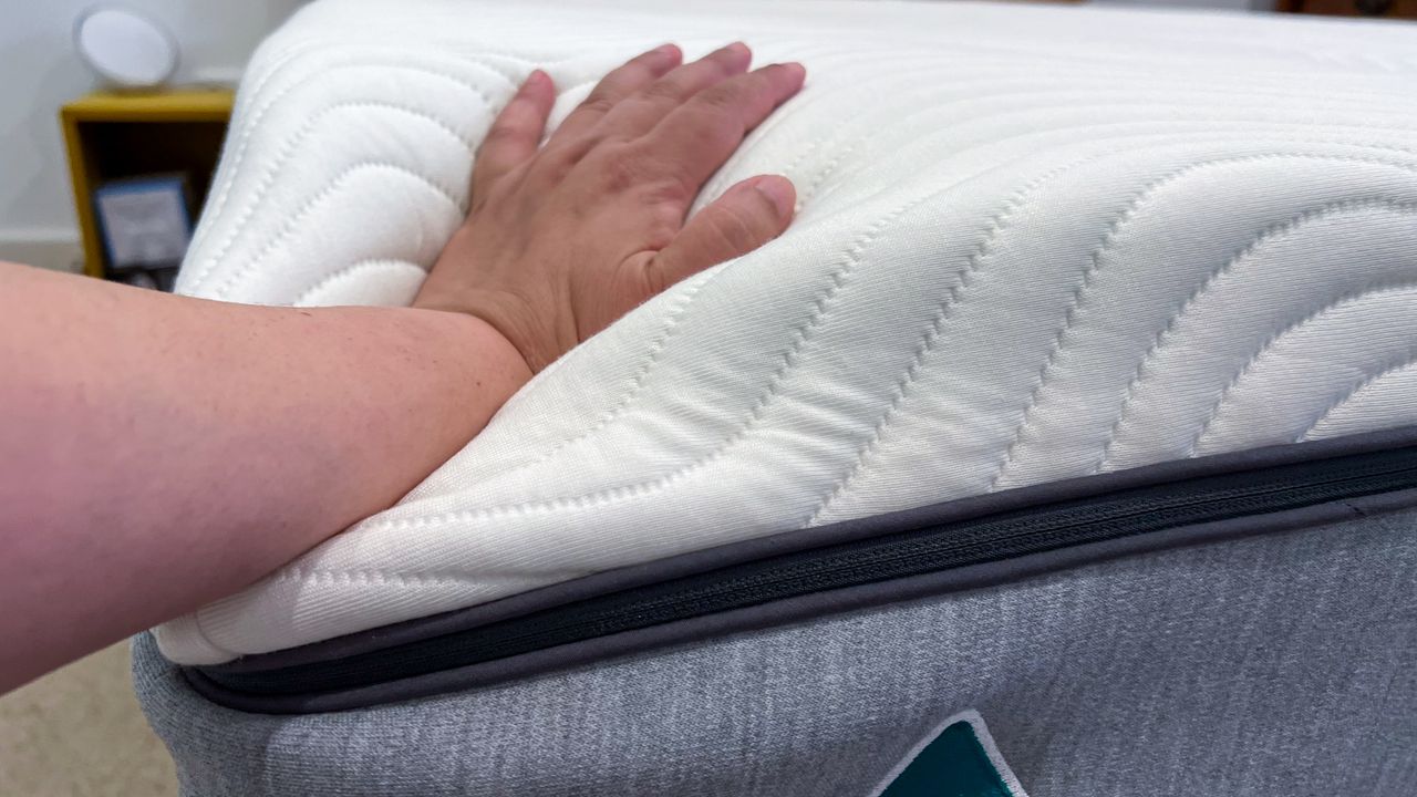 Hand pressing down on a corner of the Emma Comfort Mattress
