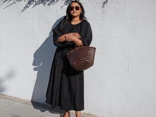 Chiara wears black dress while holding a large brown straw tote.
