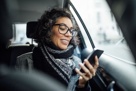 Businesswoman using phone while traveling by a taxi.