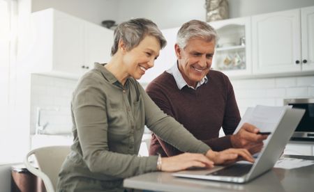 Laptop, budget and finance with a senior couple at a table in their home together for retirement planning. Computer, investment or savings with an elderly husband and wife accounting for the future