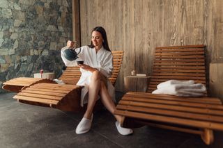 Young woman in spa robe pouring tea sat on spa recliner