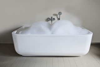 A large white, free-standing bathtub overflowing with bubbles.