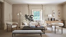 A neutral living room with white boucle furniture and a large black coffee table. On the table is a large white vase with green leafy stems.