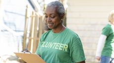 An older woman wearing a T-shirt that says "volunteer" looks at a clipboard.
