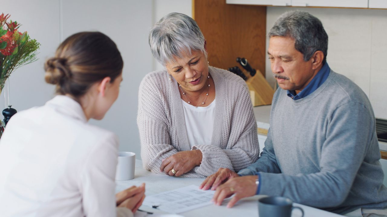 A woman and an older couple look at paperwork together at a table.