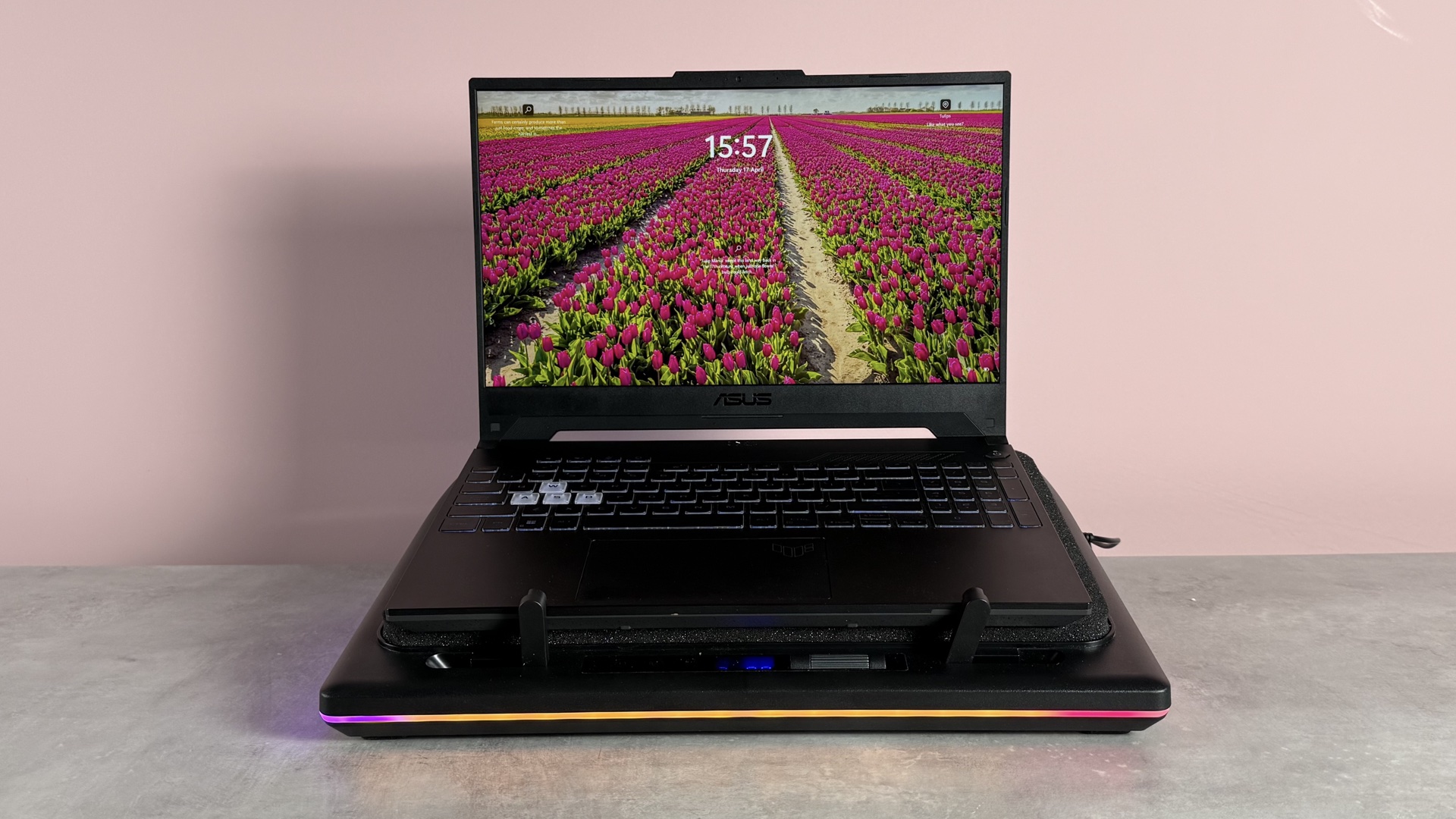 The Llano RGB Laptop Cooling Pad with a laptop on it in front of a pink background.