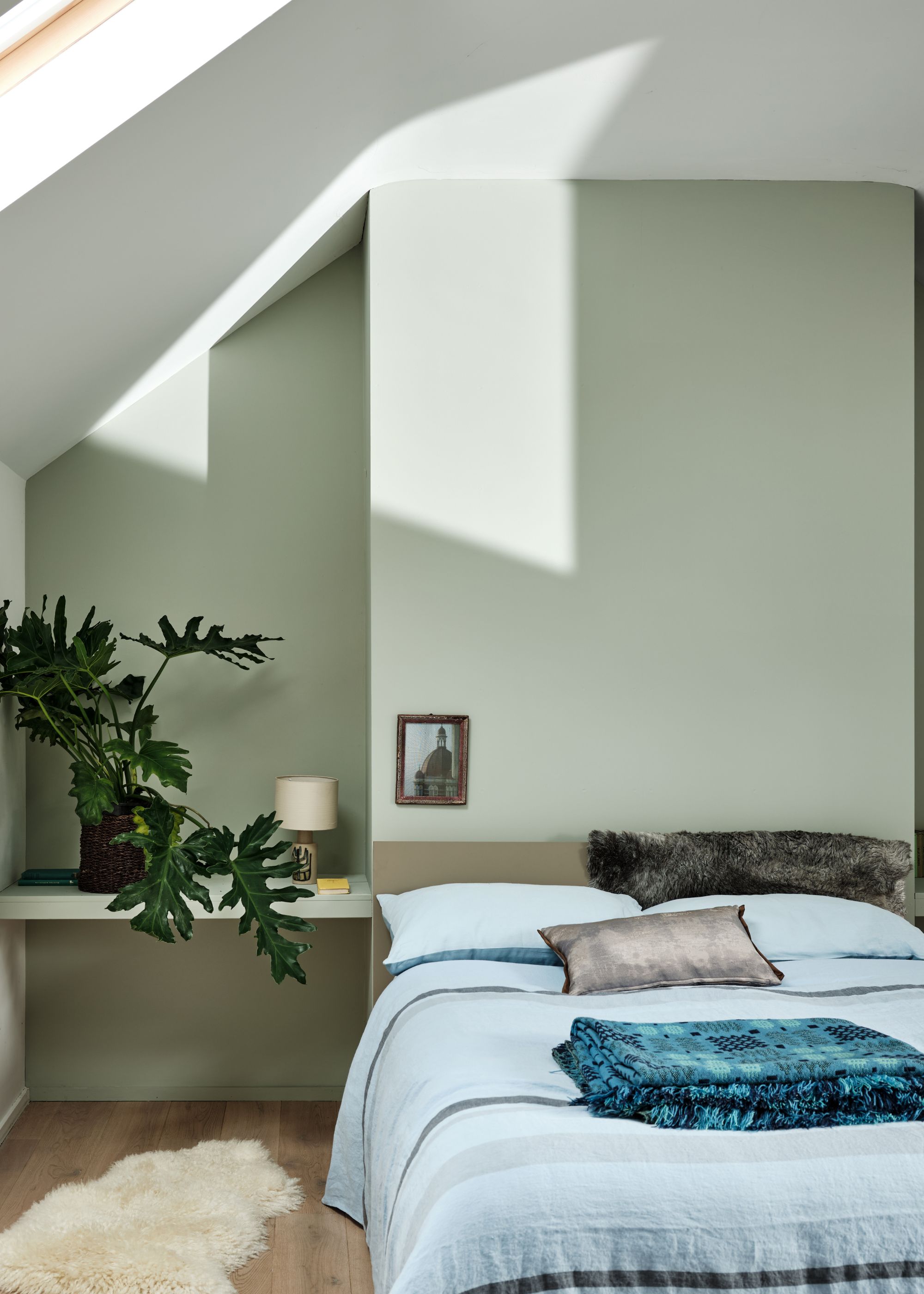 A modern bedroom with sloped ceilings and a pale green wall, pale blue bedding.