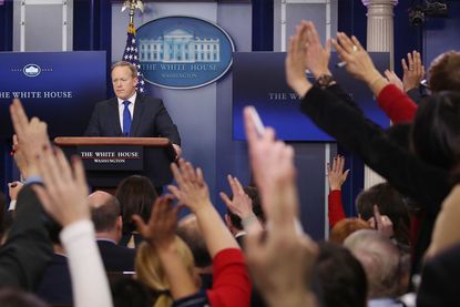 Sean Spicer confronts a room of reporters with raised hands.