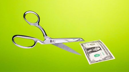 Stainless steel scissors in mid air about to cut US $1 dollar bill over gradated green background