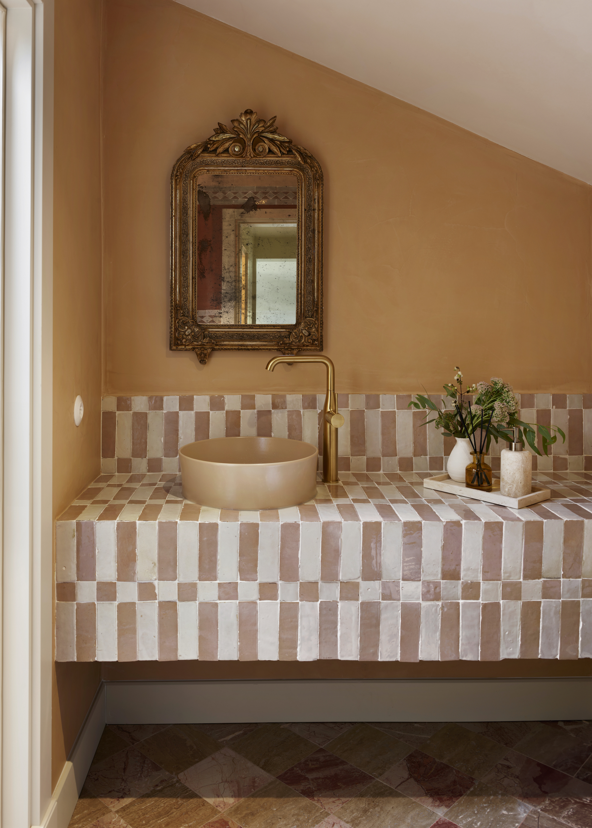 bathroom with a tiled vanity around the sink. There is a mirror hanging above the sink and on the vanity is a tray with a plant and soap on top