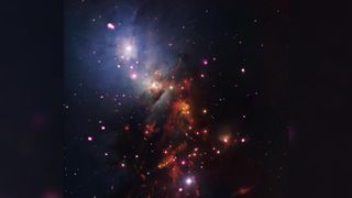 Image of NGC 1333 in the Perseus constellation. A brighter violet and white hazy patch of star filled sky is in the upper left corner of the image. Towards the lower right the color of the gas and dust turns a darker brown/red.