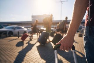 Group of people walking to airport terminal at summer sunset. Selective focus on the hand of a man with a suitcase