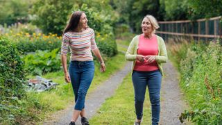 Two women walking down a country lane in nature together, laughing together and talking