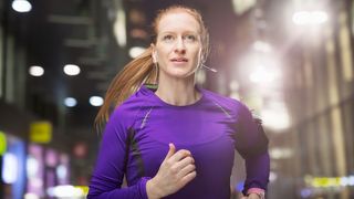 A woman with red hair wearing a purple top jogging through the city at night