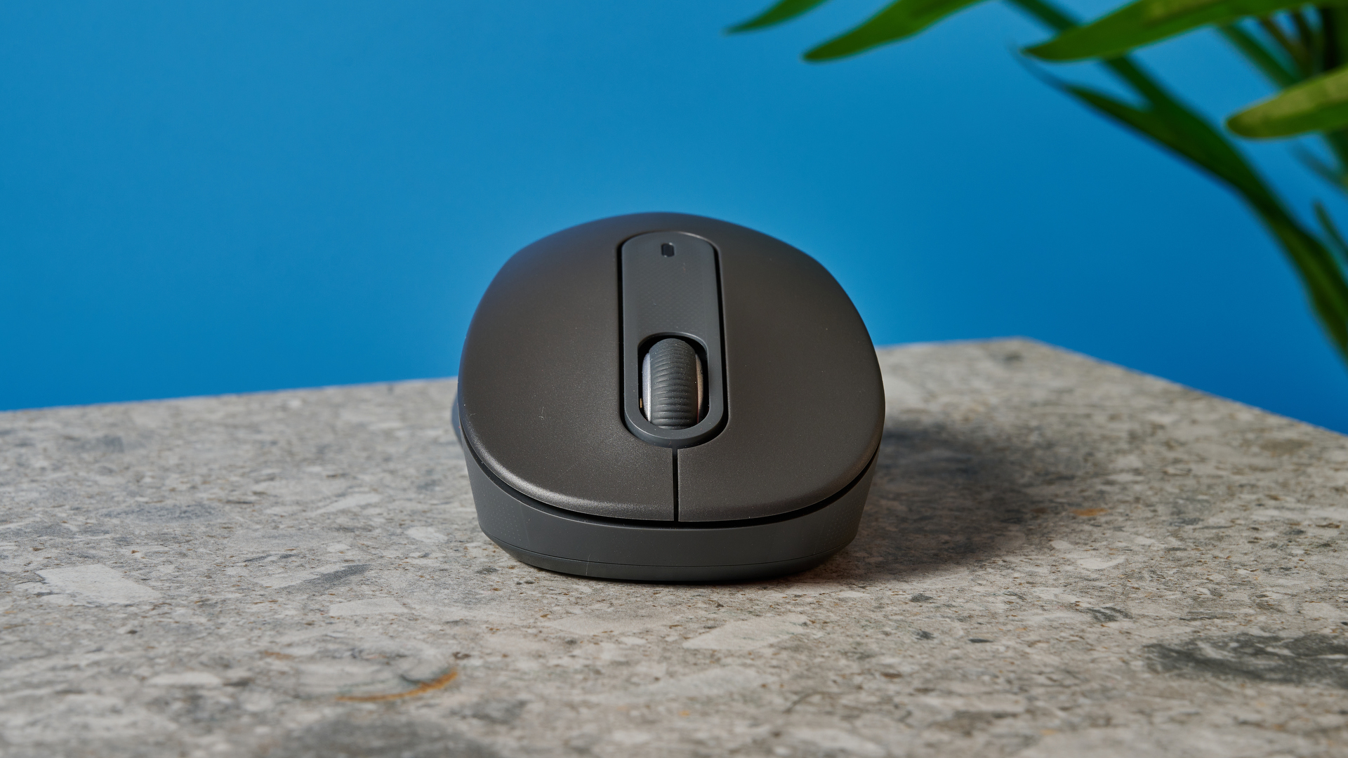 a black mouse with a scroll wheel, two side buttons, and grooved edges, with a logi logo, sits atop a pale table with a blue background