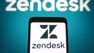 The Zendesk logo on a smartphone with the name of the company on a wall behind it