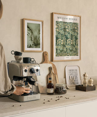 A neutral kitchen with metallic coffee machine and green art prints