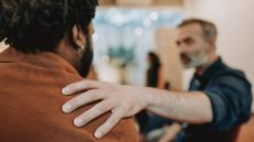 A man places his hand on another man's shoulder in support