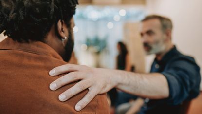 A man places his hand on another man's shoulder in support