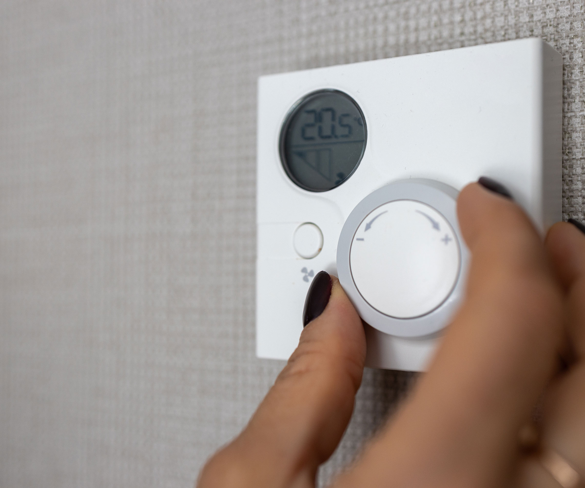 woman's hand adjusting wall mounted thermostat