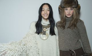 2 Models wearing white poncho with necklace and brown jersey with belt and fur headwear