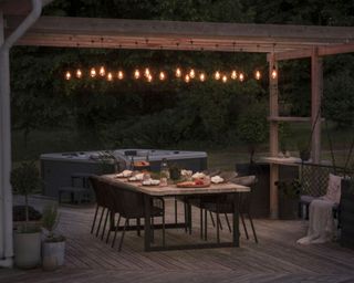 festoon lights hanging from a wooden pergola over a dining area