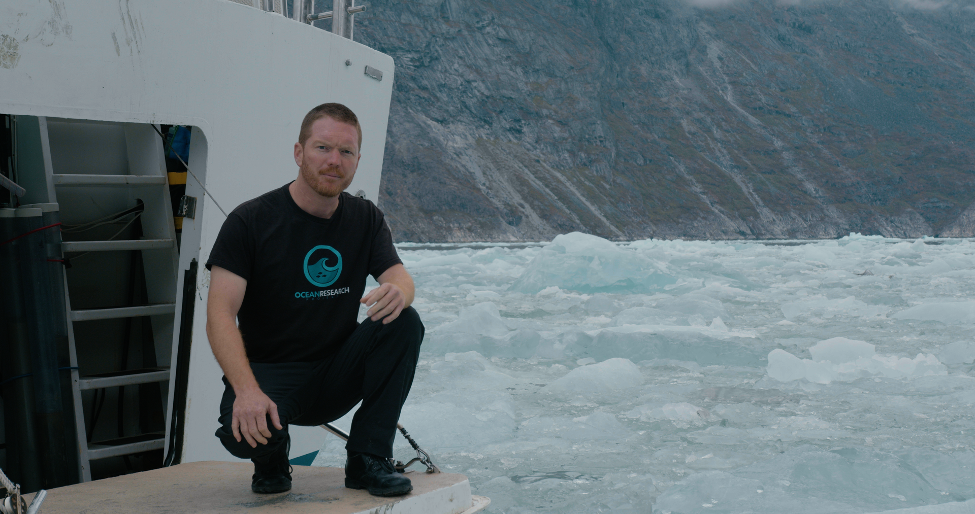 A man squats on the deck of a ship in an icy ocean