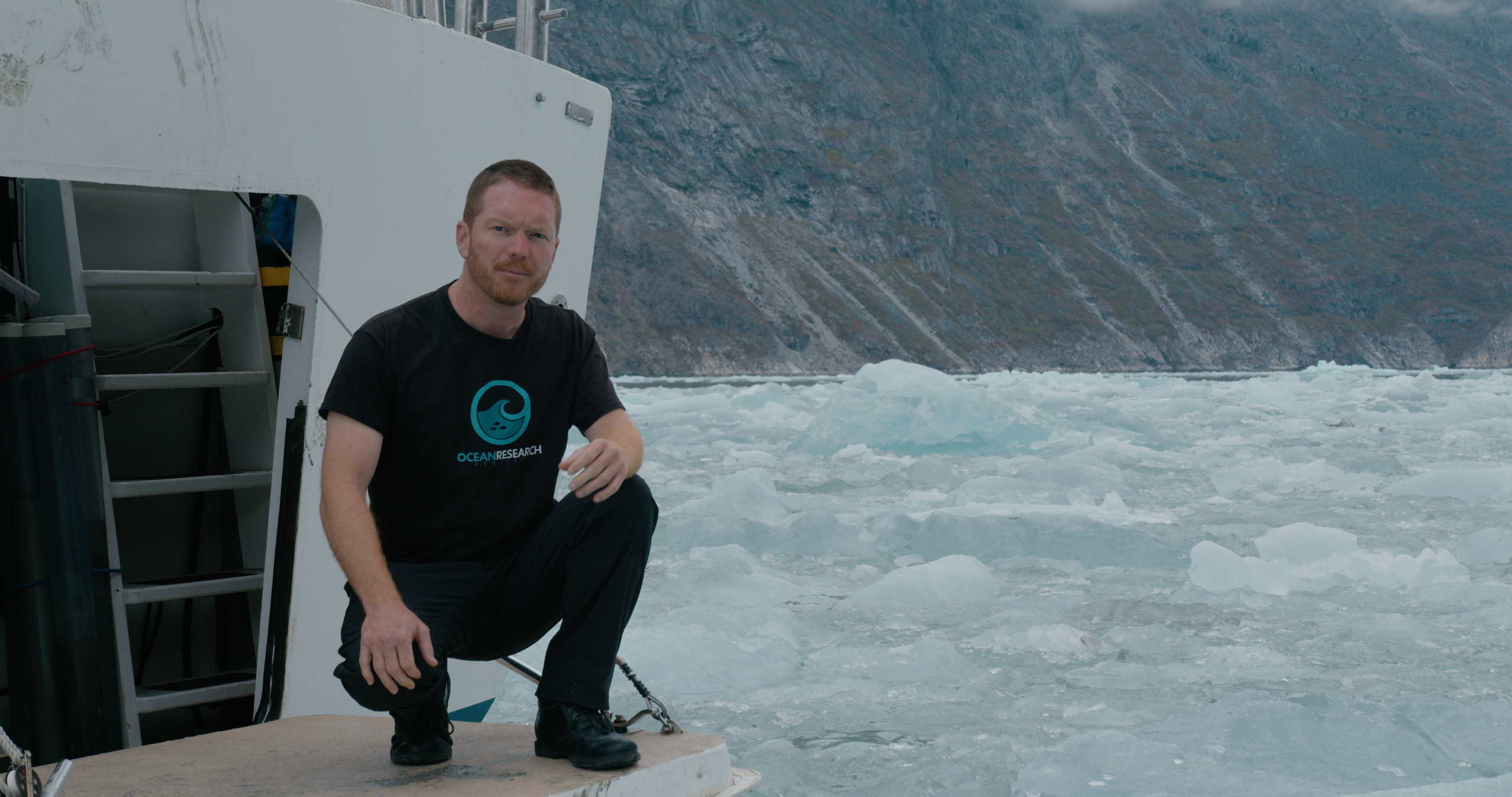 A man squats on the deck of a ship in an icy ocean