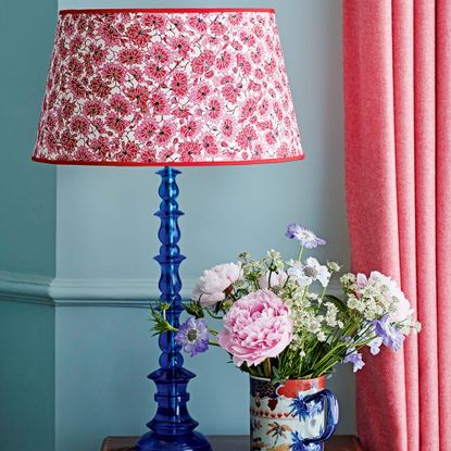 Floral fabric lampshade on blue base next to mug of flowers