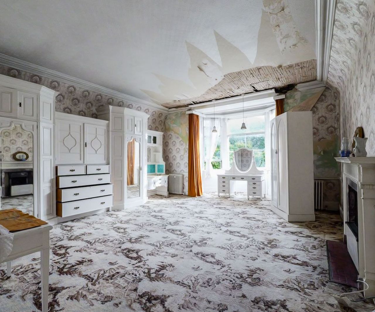 An empty bedroom except white furniture and fireplace with white wallpaper peeling