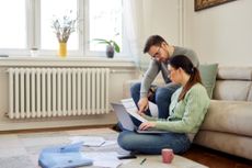 A young couple sit in their living room while reviewing paperwork and discussing their budget.