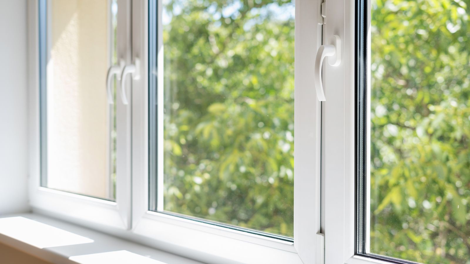 A new plastic pvc window with white metal frame installed at modern house, view of blurred green trees.