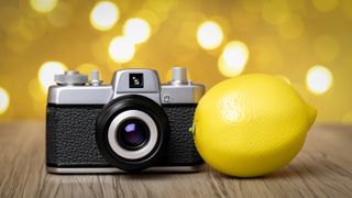A camera next to a lemon on a wooden surface, with a blurry background and bokeh balls