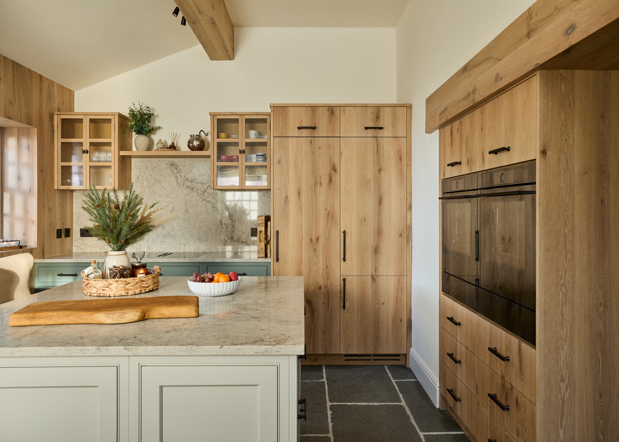 an oak kitchen with a contrasting kitchen island. On the island is a marble countertop and a chopping board, as well as a bowel of fruit and tray of essentials.