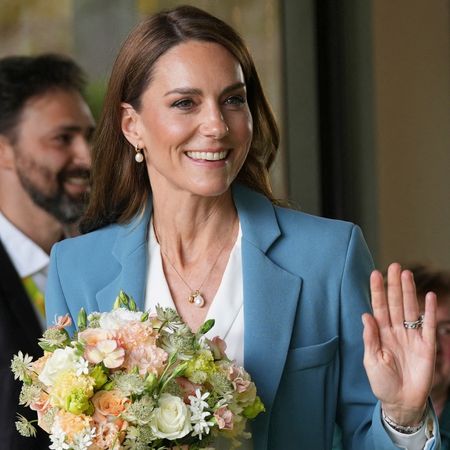Princess Kate wearing a blue suit, holding flowers and waving