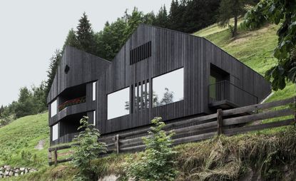Exterior view of Modern Chalet in Italy. The chalet features a vertical wooden plank design, large windows and it is surrounded by greenery