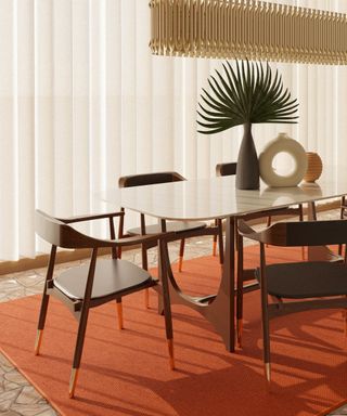 A mid-century modern dining room with a brown wooden table with a spiked leaf plant and a circular beige vase on it, four wooden chairs around it, a blood orange rug beneath it and white curtains behind it