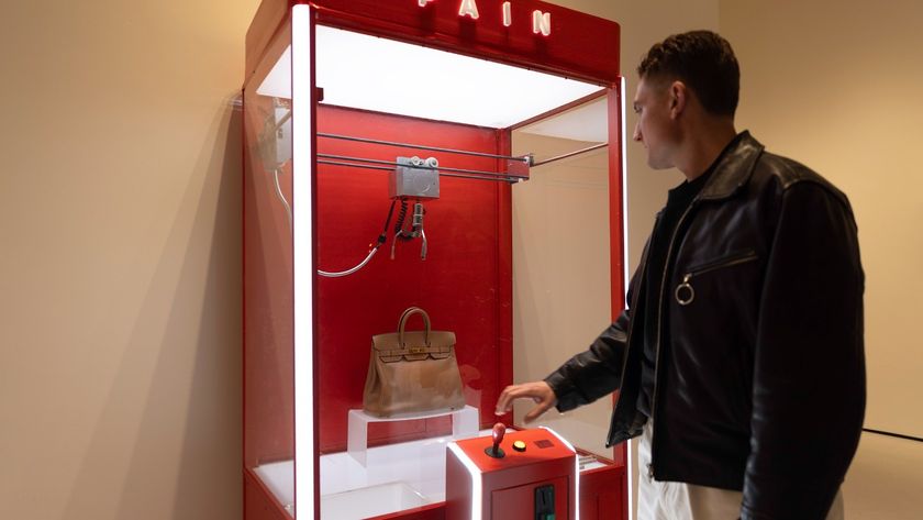 A man in a leather jacket stands before the red "PAIN" claw machine, reaching for the joystick to attempt to grab the designer handbag inside.