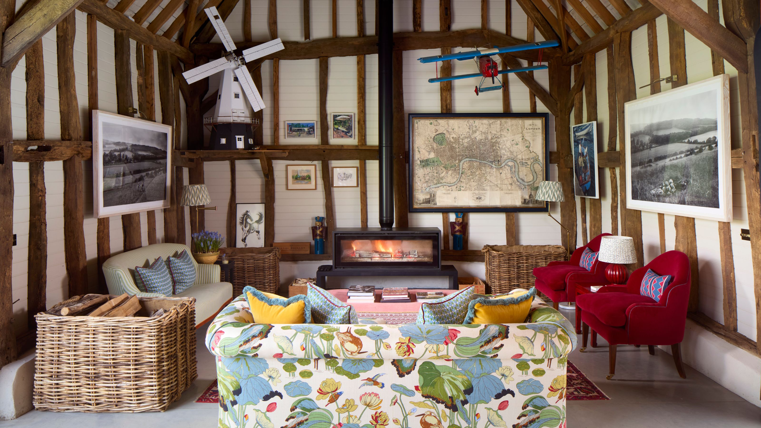 a rustic beamed barn conversion with a fireplace, vintage windmill, patterned sofa and two red armchairs