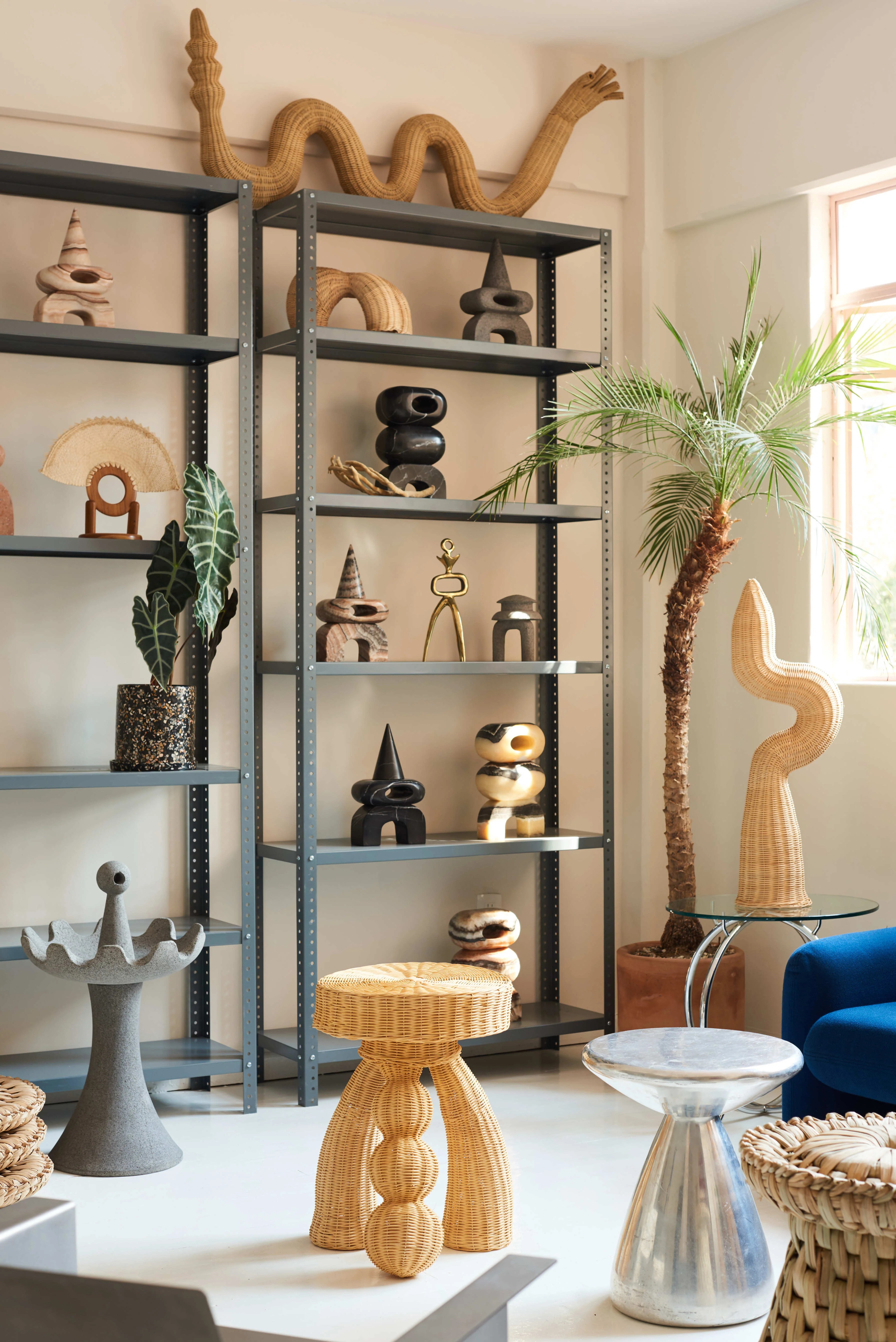 A showroom with metallic shelving units filled with sculptural objects with an abstract or creaturesque pieces, along with plants.