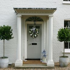 A front porch with a grey front door decorated with a white flower wreath and two white lanterns on the floor