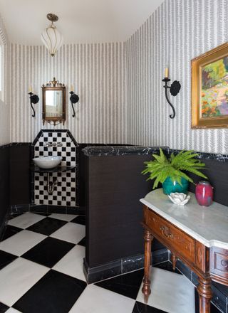 traditional style bathroom with black and white marble floor tiles and monochrome striped wallpaper and marble topped console