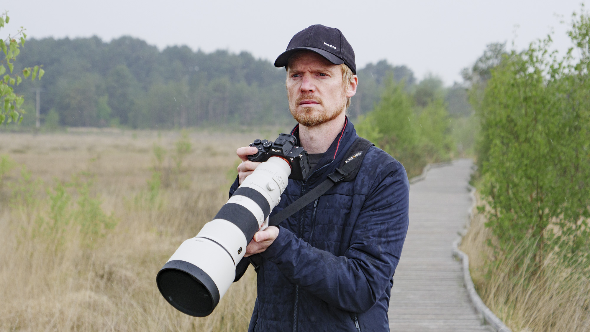 Man holding the Sony FE 400-800mm F6.3-8 G OSS supertelephoto zoom lens, he's standing on a boardwalk in a nature reserve