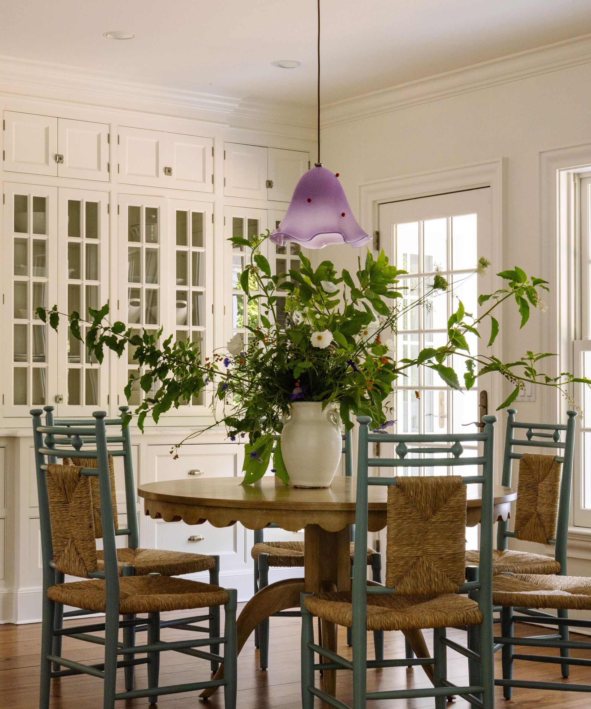 Breakfast nook with built in cupboards, round dining table and green wicker chairs with purple low pendant light