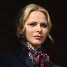 Princess Charlene wears a silk scarf and coat and wears her hair tied back