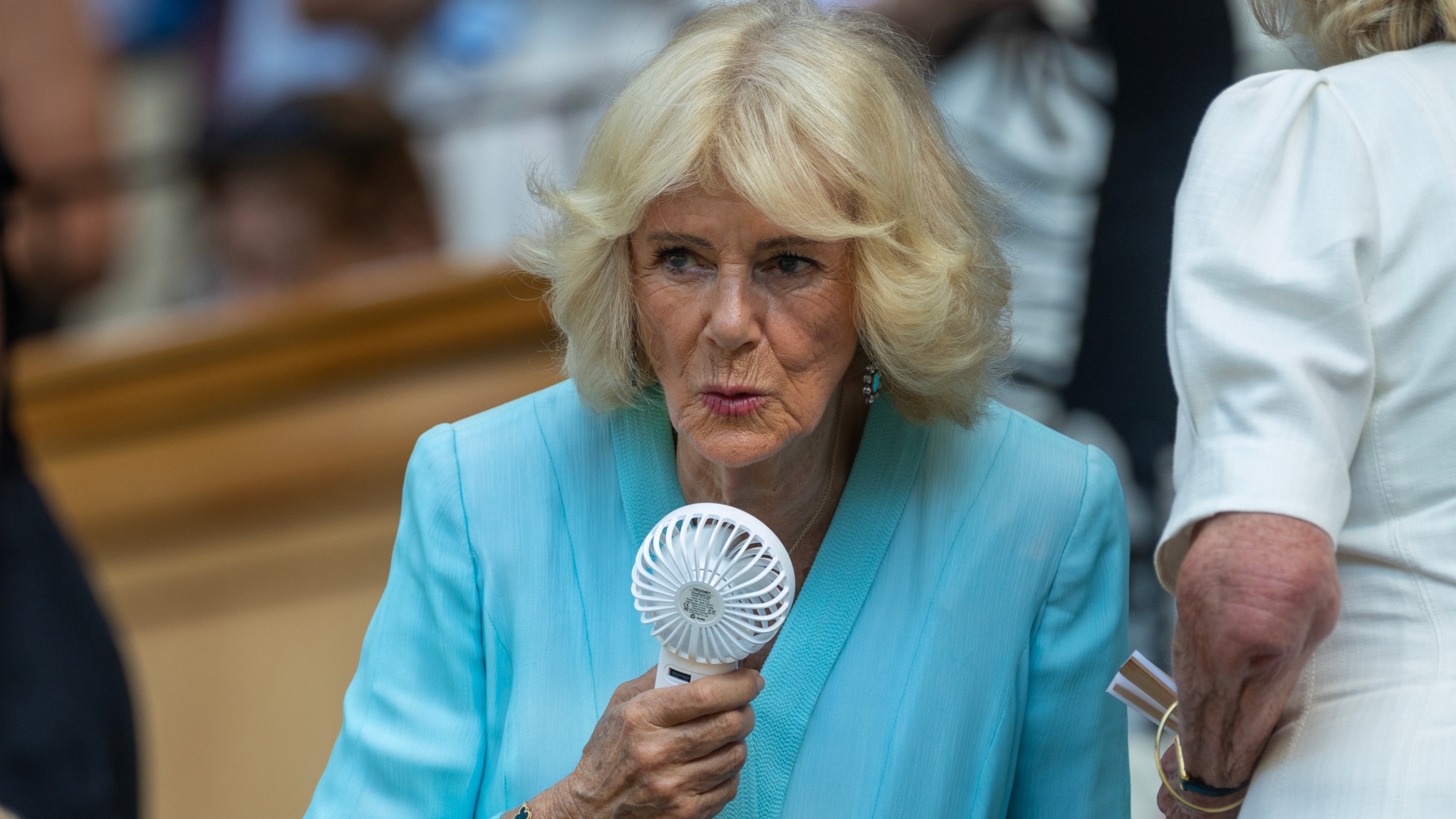 Queen Camilla cools off with a small fan in the Royal Box on Centre Court during Wimbledon on July 8th, 2026
