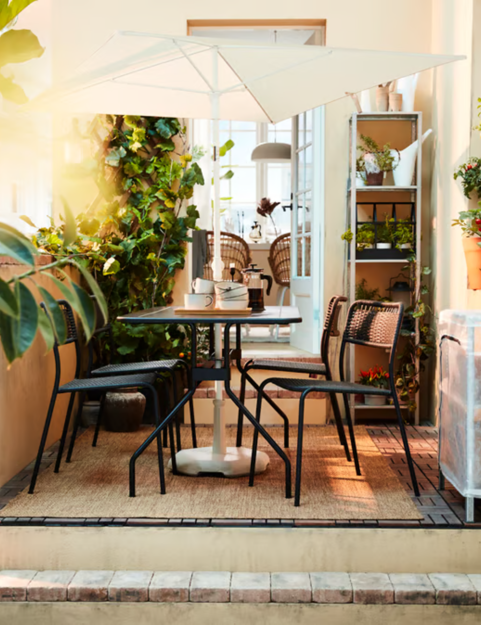 IKEA's space-saving $35 TVET&amp;Ouml; umbrella shading a charming black iron patio dining set atop of a small patio accented with potted plants