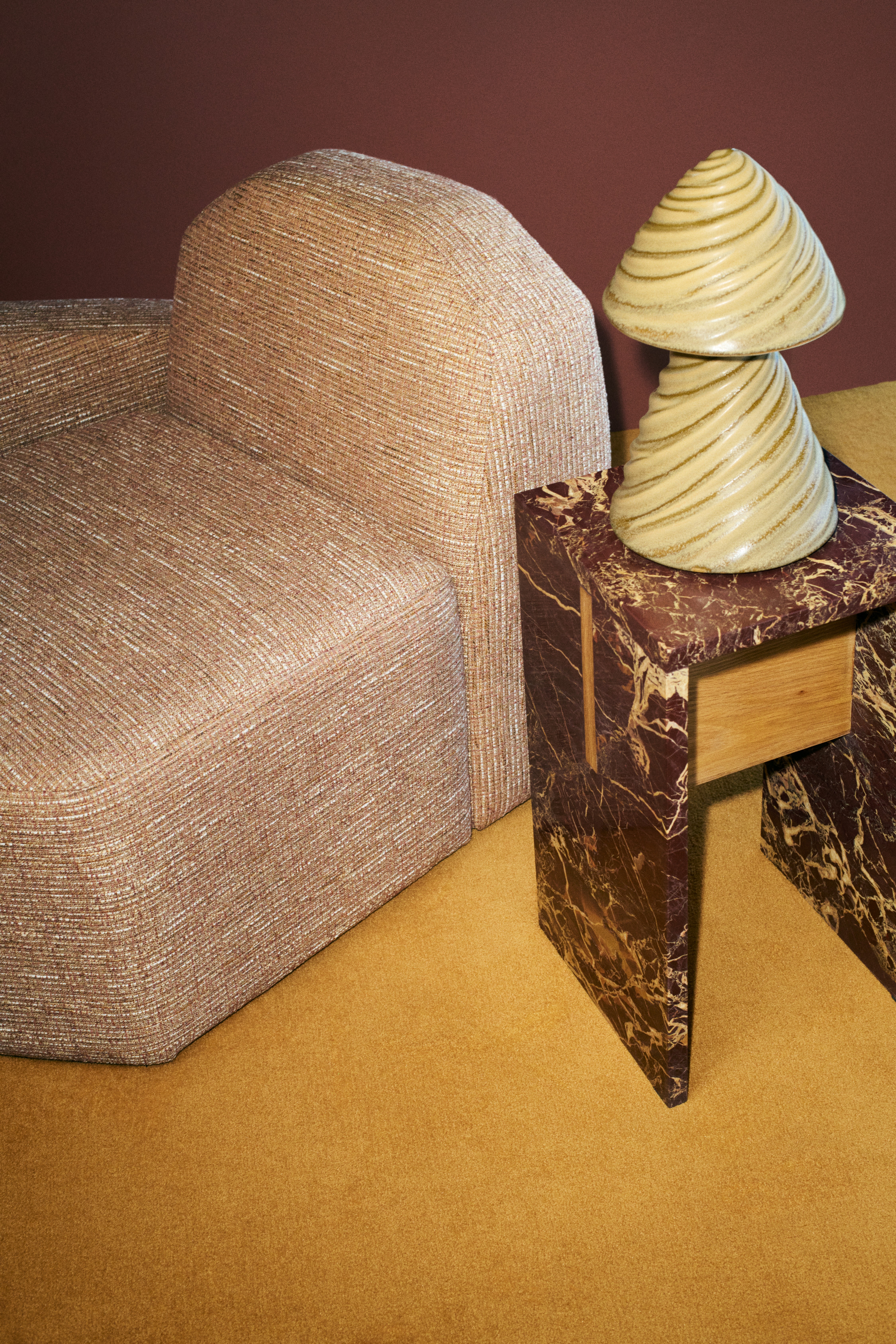 Installation shots of sculpturally designed pieces, including vases, coffee tables, armchairs, and black-and-white clothing hung up on a bordeaux rail in rooms with red or ochre carpet.