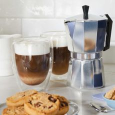 Stovetop espresso maker and two cups of coffee on kitchen worktop