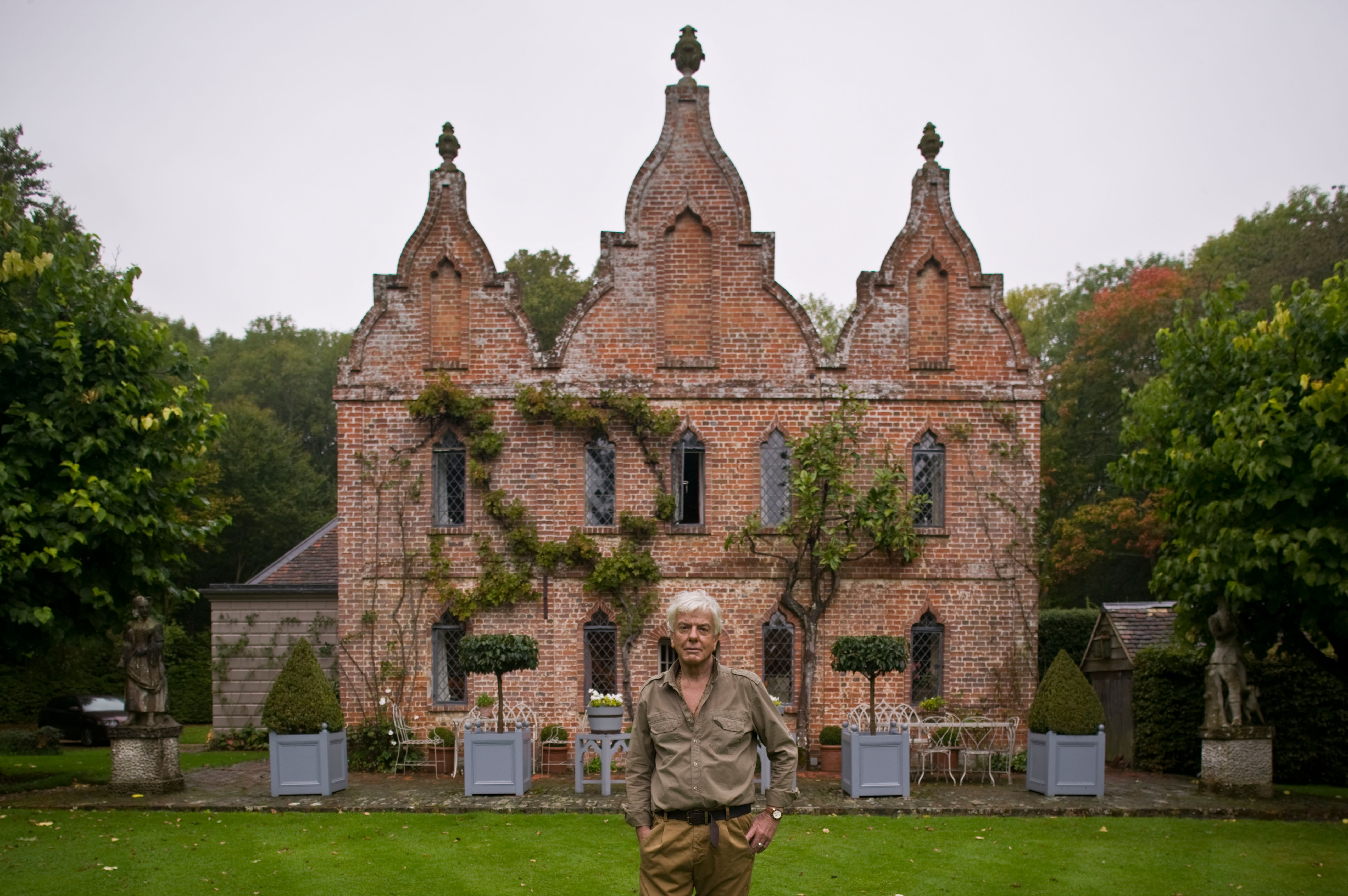Nicky Haslam standing infront of a red brick Queen Anne house in Hampshire